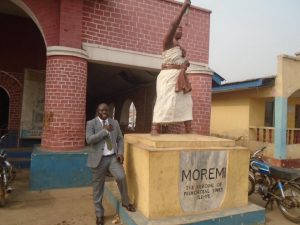 Bayo Adeyinka posing beside the Moremi statue in Ile Ife, honoring the heroine of primordial times.